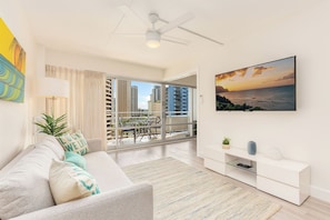 A modern living room with a sofa, a TV, and a balcony with a city view. - Renovated City Suite at Ilikai Steps to the Beach & Short Walk to Restaurants (Honolulu)