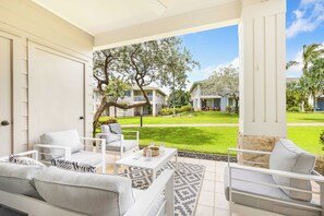 A patio with white furniture, a patterned rug, and a view of a well-maintained lawn and houses in the background. - Luxury 2 Story Ko Olina Retreat With Resort Amenities Near Lagoons (Kapolei)