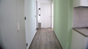 A narrow hallway with a door at the end, a light switch on the wall, and a small trash bin. - Solferino Light & Space | Central Turin (Torino)