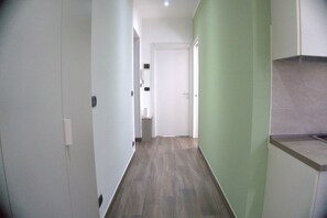 Un corridoio stretto con una porta in fondo, un interruttore sulla parete e un piccolo cestino.