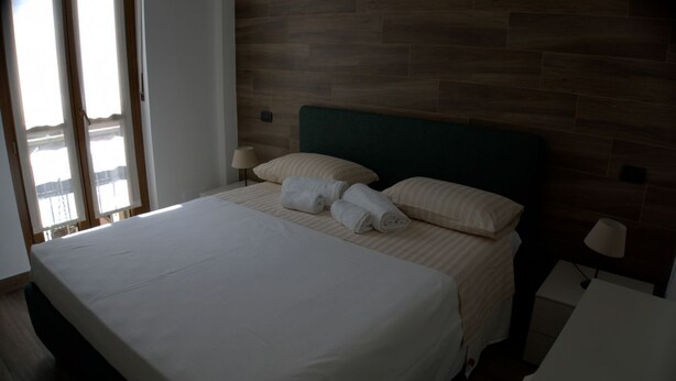 A hotel room with a large bed, two bedside lamps, a wooden headboard, and a view through a window. - Solferino Light & Space | Central Turin (Torino)