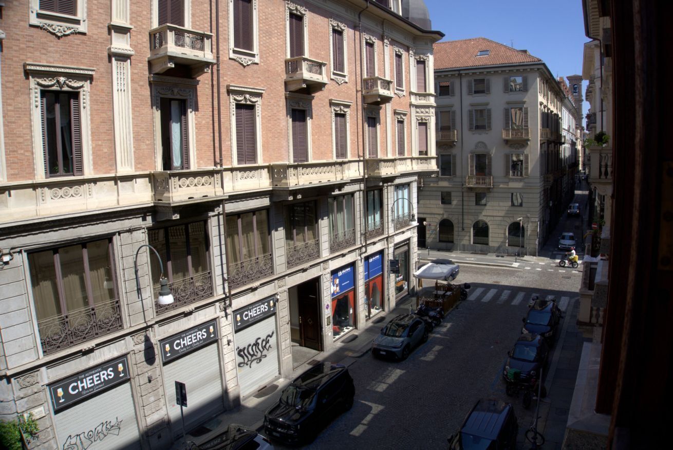 Una veduta di una strada con un edificio a più piani, caratterizzato da balconi e una fila di auto parcheggiate.
