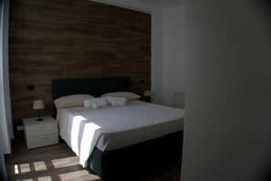 Un dormitorio con cabecera de madera, cama con ropa blanca, mesita de noche con lámpara y cajón.