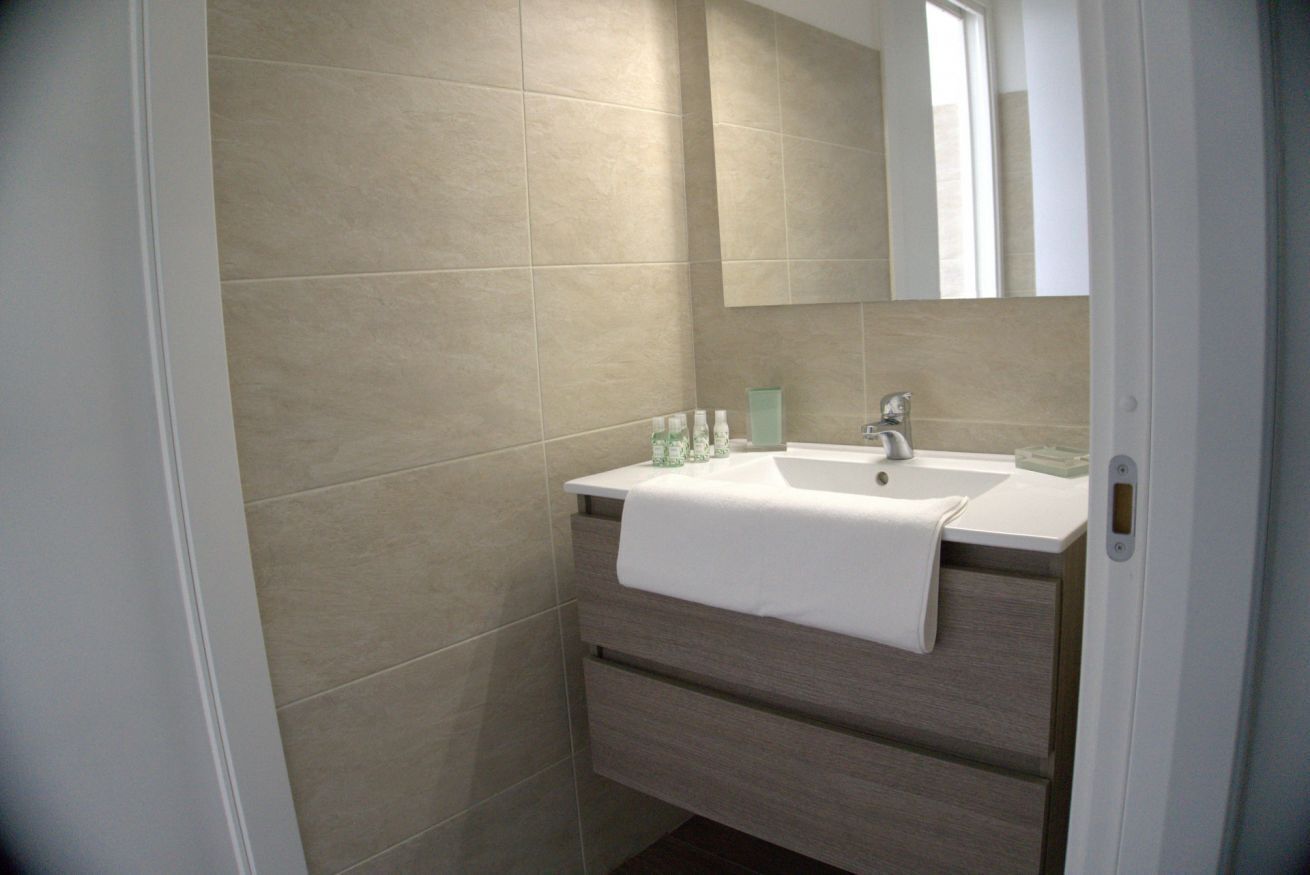 Un bagno con un lavandino bianco, uno specchio e un asciugamano appeso al muro.
