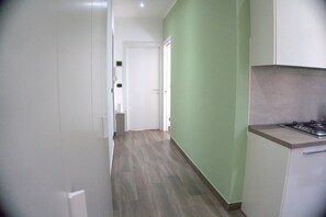 En smal hall med ett köksutrymme på höger sida, med en gasspis och skåp.