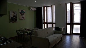 A living room with a sofa, a dining table with chairs, and a kitchen area with a stove. - Solferino Light & Space | Central Turin (Torino)