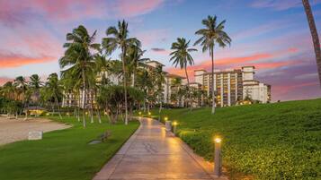 A pathway leading to a hotel with palm trees and a sunset sky.