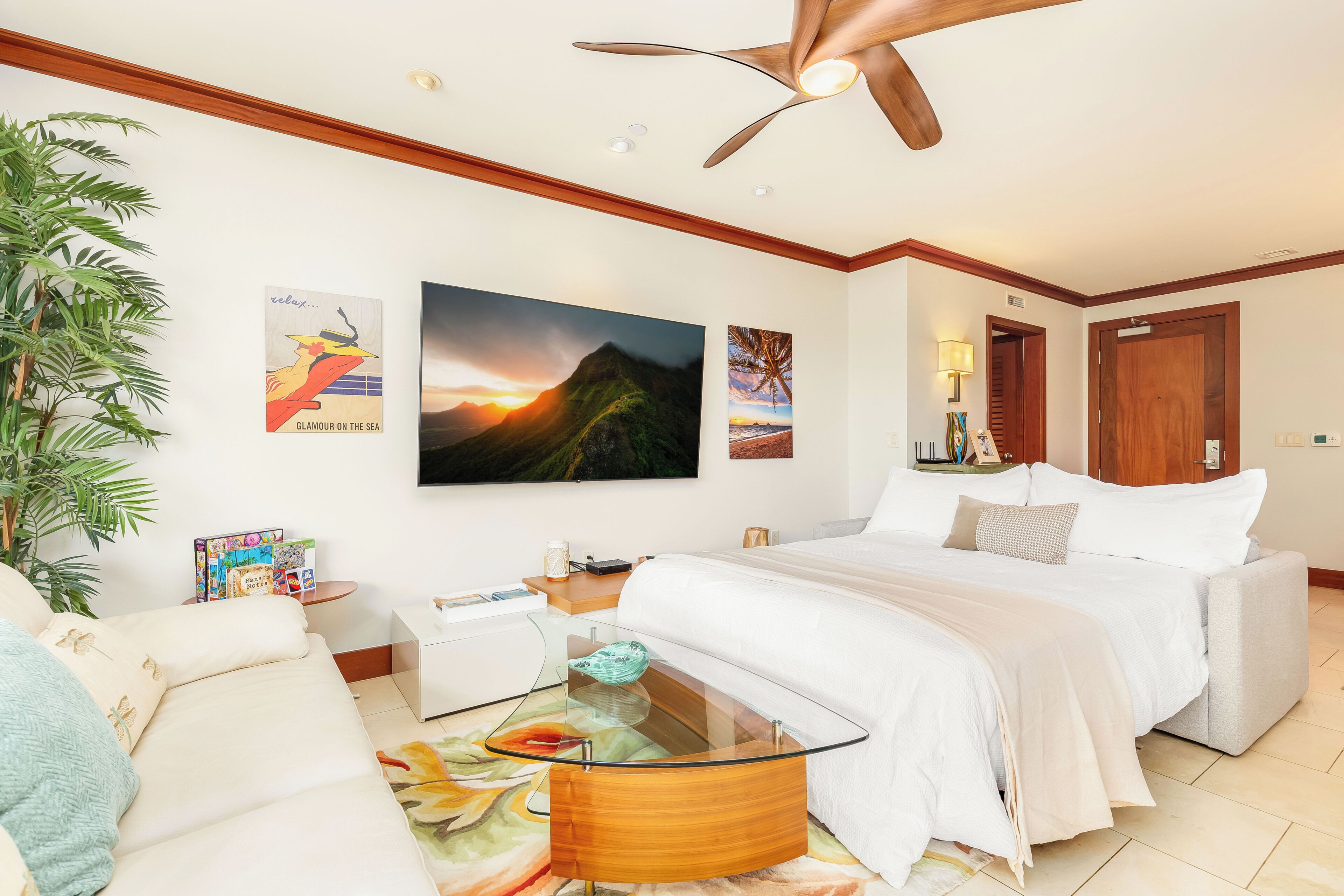 A modern hotel room with a bed, a glass coffee table, a sofa, and a ceiling fan.