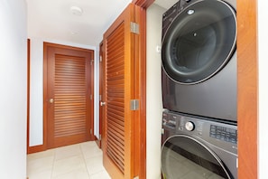 A laundry room with a stacked washer and dryer, a wooden door, and a tiled floor.