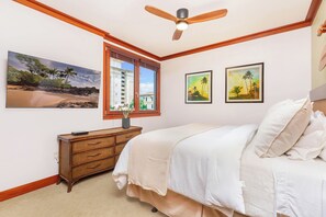 A bedroom with a bed, a dresser, a window with a view of a building, and two framed pictures on the wall.