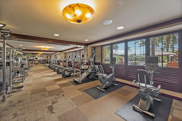 A gym with various exercise machines, a checkered floor, and large windows with blinds.