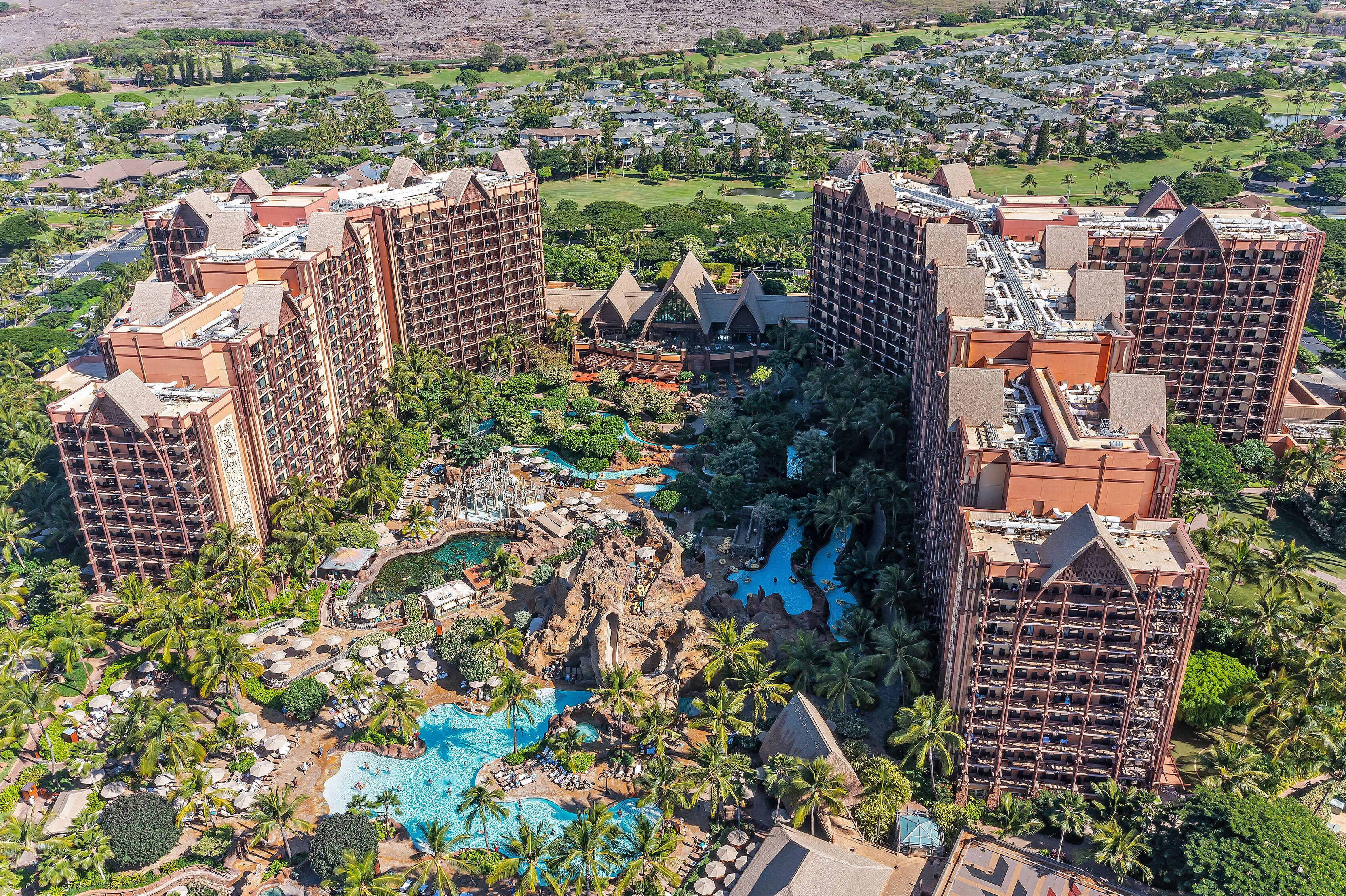 A resort with multiple high-rise buildings, a central pool area with palm trees, and a golf course in the background.