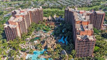 A resort with multiple high-rise buildings, a central pool area with palm trees, and a golf course in the background.