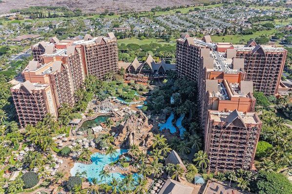 A resort with multiple high-rise buildings, a central pool area with palm trees, and a golf course in the background.