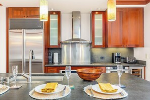A modern kitchen with stainless steel appliances, wooden cabinets, and a central island with a large bowl and wine glasses.