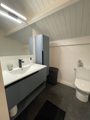Une salle de bain moderne avec un lavabo blanc, un miroir, des toilettes et une poubelle.