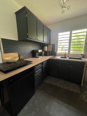 A modern kitchen with black cabinets, a coffee maker, and a dishwasher. - House with a pool (Sainte-Anne)