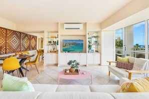 A modern living room with a dining area, a large flat-screen TV, and a view of the ocean. - Beachfront Property W/sand Access at Waikiki Shore Condo With Full Kitchen (Honolulu)
