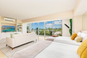 A modern hotel room with a large balcony, a sofa, two beds, and a television. - Beachfront Property W/sand Access at Waikiki Shore Condo With Full Kitchen (Honolulu)