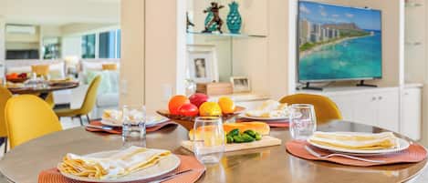Un coin repas avec une table ronde dressée pour deux personnes, comprenant des assiettes, des couverts et un verre d’eau.