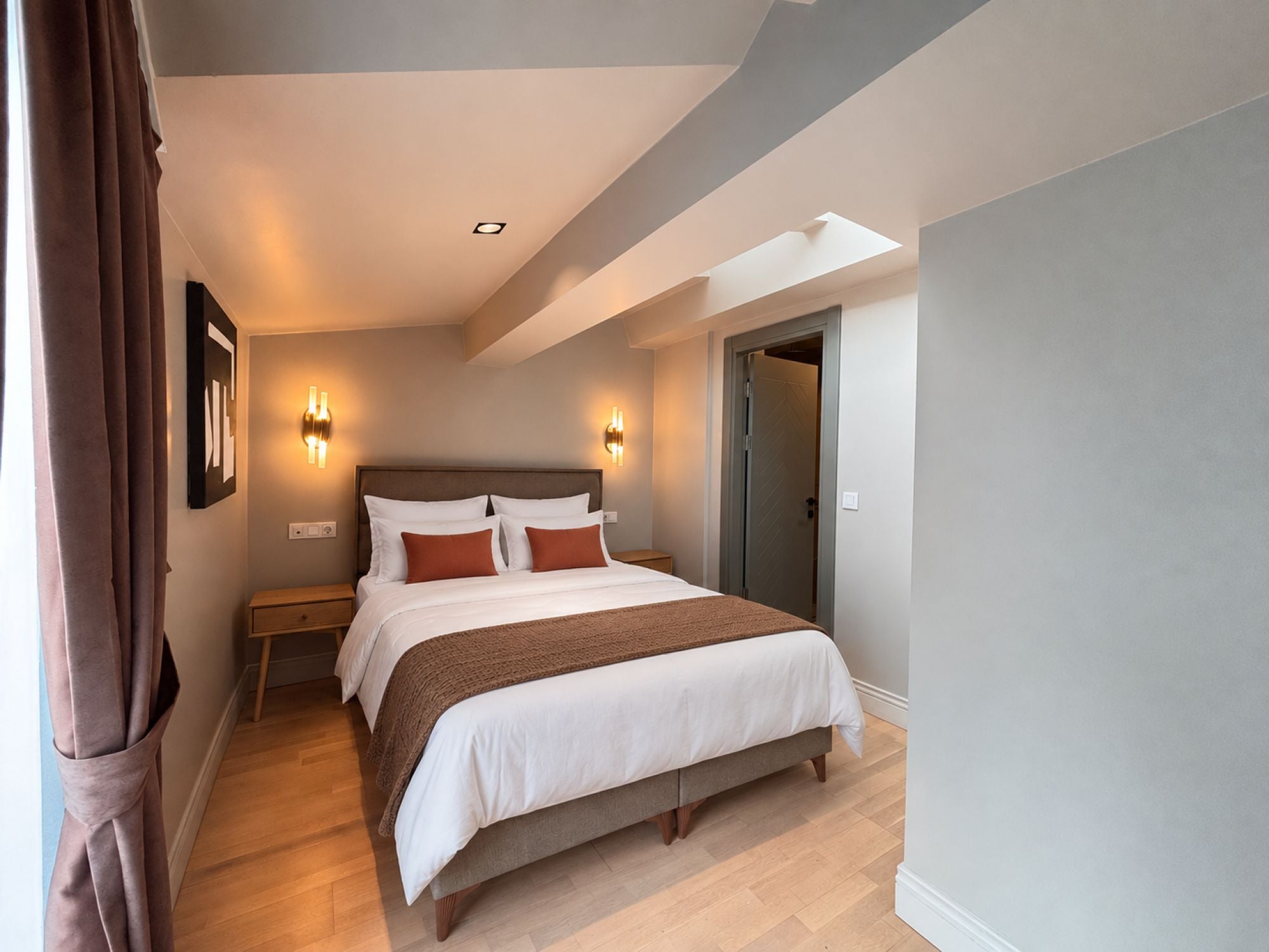 A hotel room with a large bed, bedside tables, a wardrobe, and a door leading to another room.