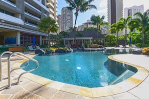 A hotel pool area with a clear pool, lounge chairs, and palm trees. - Ocean-sunset Views Designer Condo at The Watermark W/great Building Amenities (Honolulu)