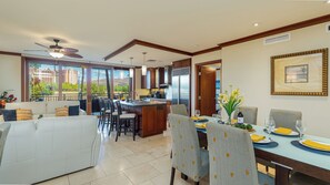 A spacious living area with a dining table set for four, a kitchen with modern appliances, and large windows offering a view of the cityscape. - Beach Villas Peekaboo Ocean & Mountain View Resort W/luxurious Amenities (Kapolei)