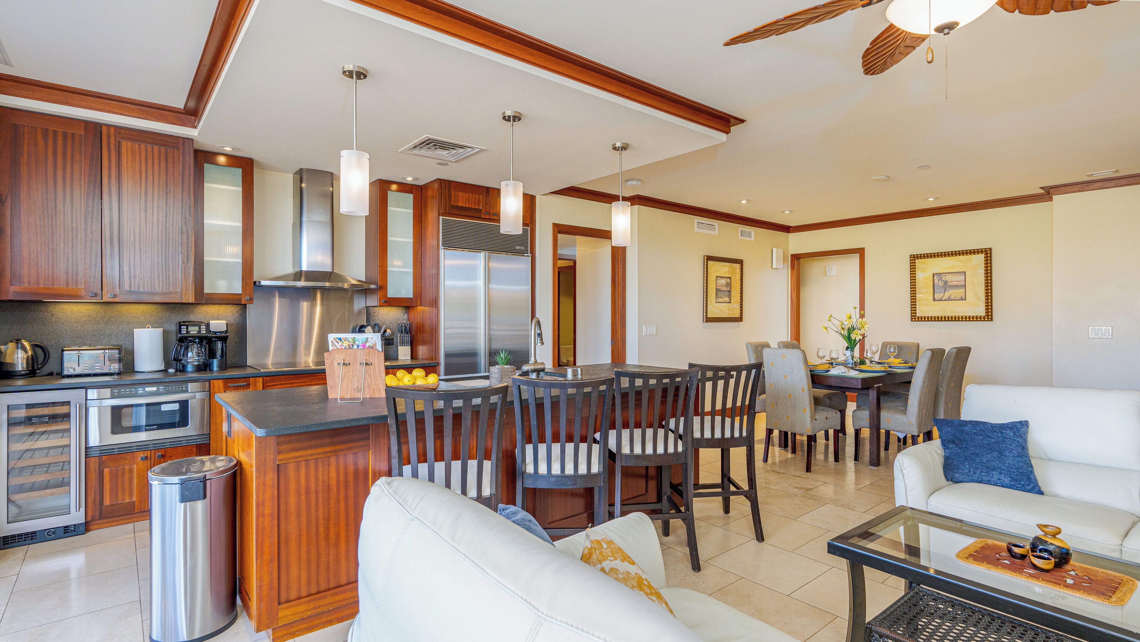 A modern kitchen with stainless steel appliances, wooden cabinets, and a dining area with a white sofa and a glass coffee table.