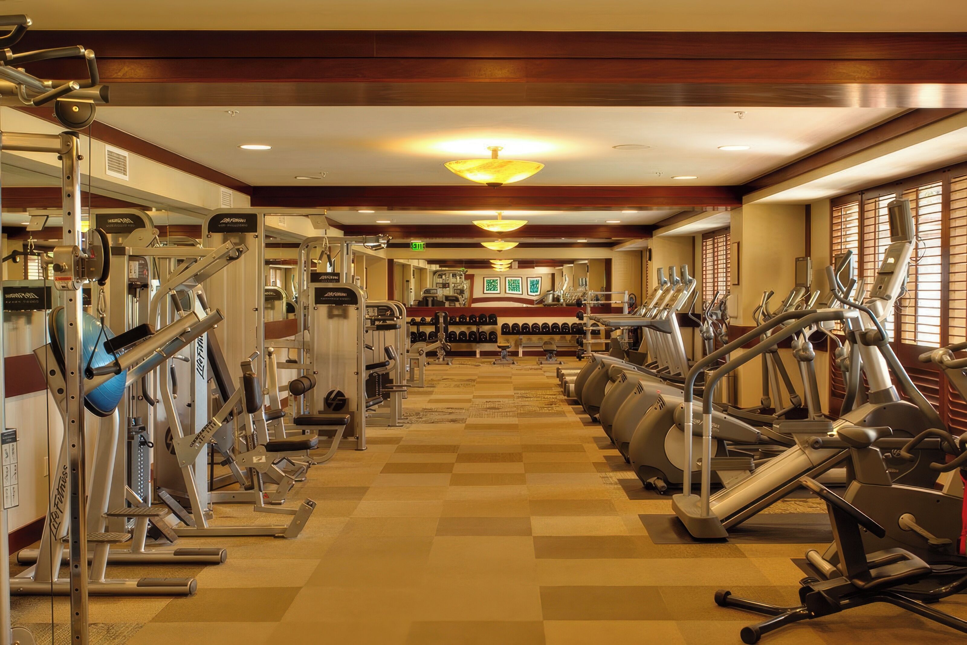 A gym with various exercise machines, a central mirror, and a checkered floor.