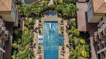 An aerial view of a hotel with a central swimming pool surrounded by lush landscaping and multiple balconies.