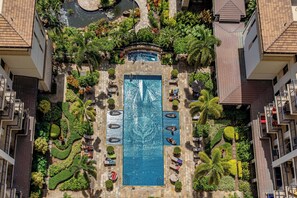An aerial view of a hotel with a central swimming pool surrounded by lush landscaping and multiple balconies.