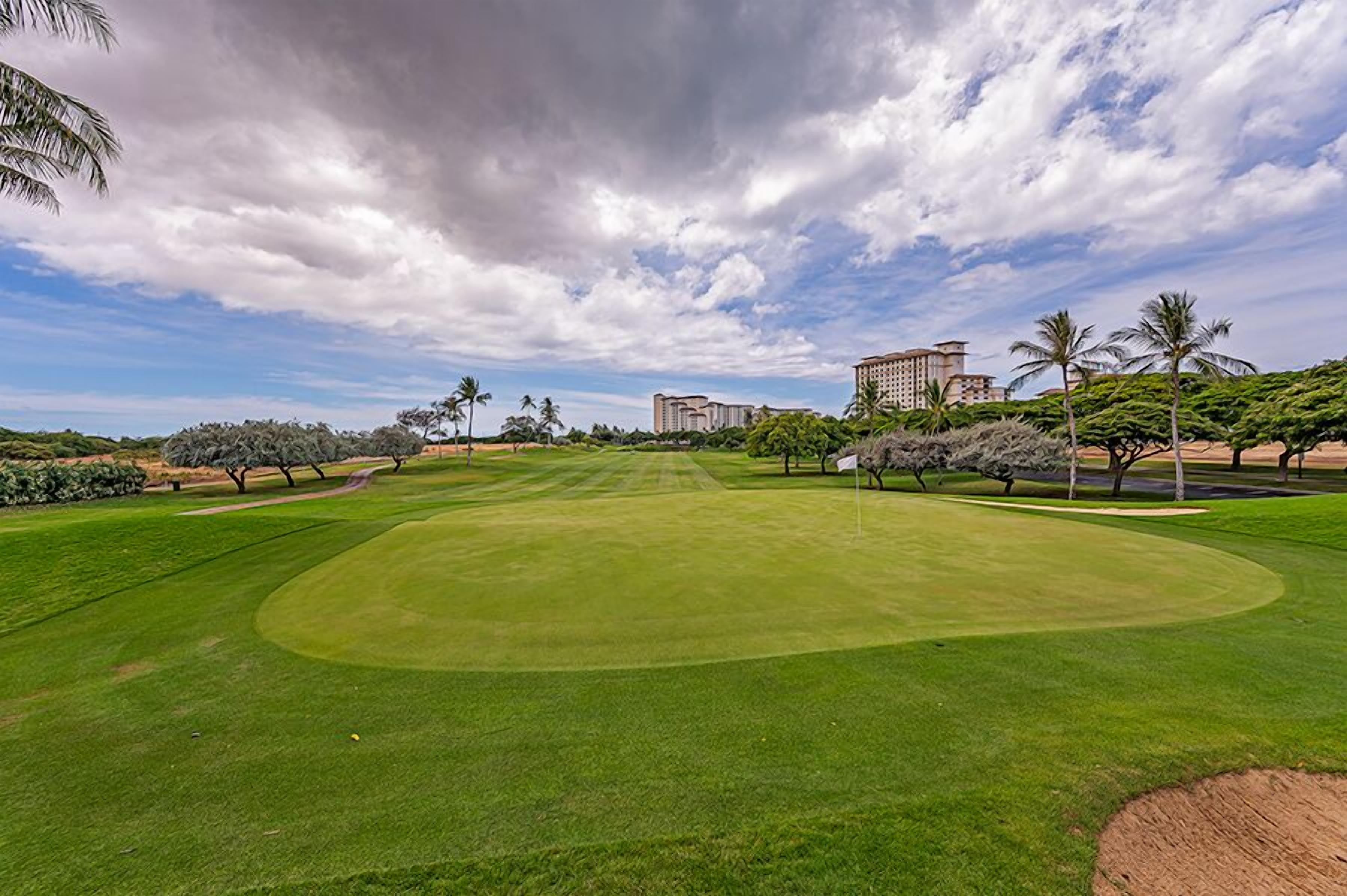A well-maintained golf course with a clear sky, palm trees, and modern buildings in the background.