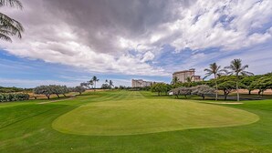 Ein gepflegter Golfplatz bei strahlend blauem Himmel, mit Palmen und modernen Gebäuden im Hintergrund.