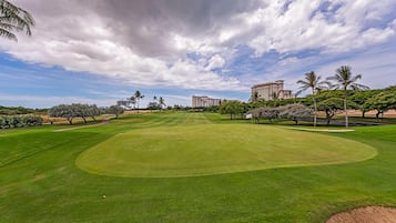 A well-maintained golf course with a clear sky, palm trees, and modern buildings in the background.