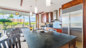 A modern kitchen with a large island, stainless steel appliances, and a view of a tropical landscape.