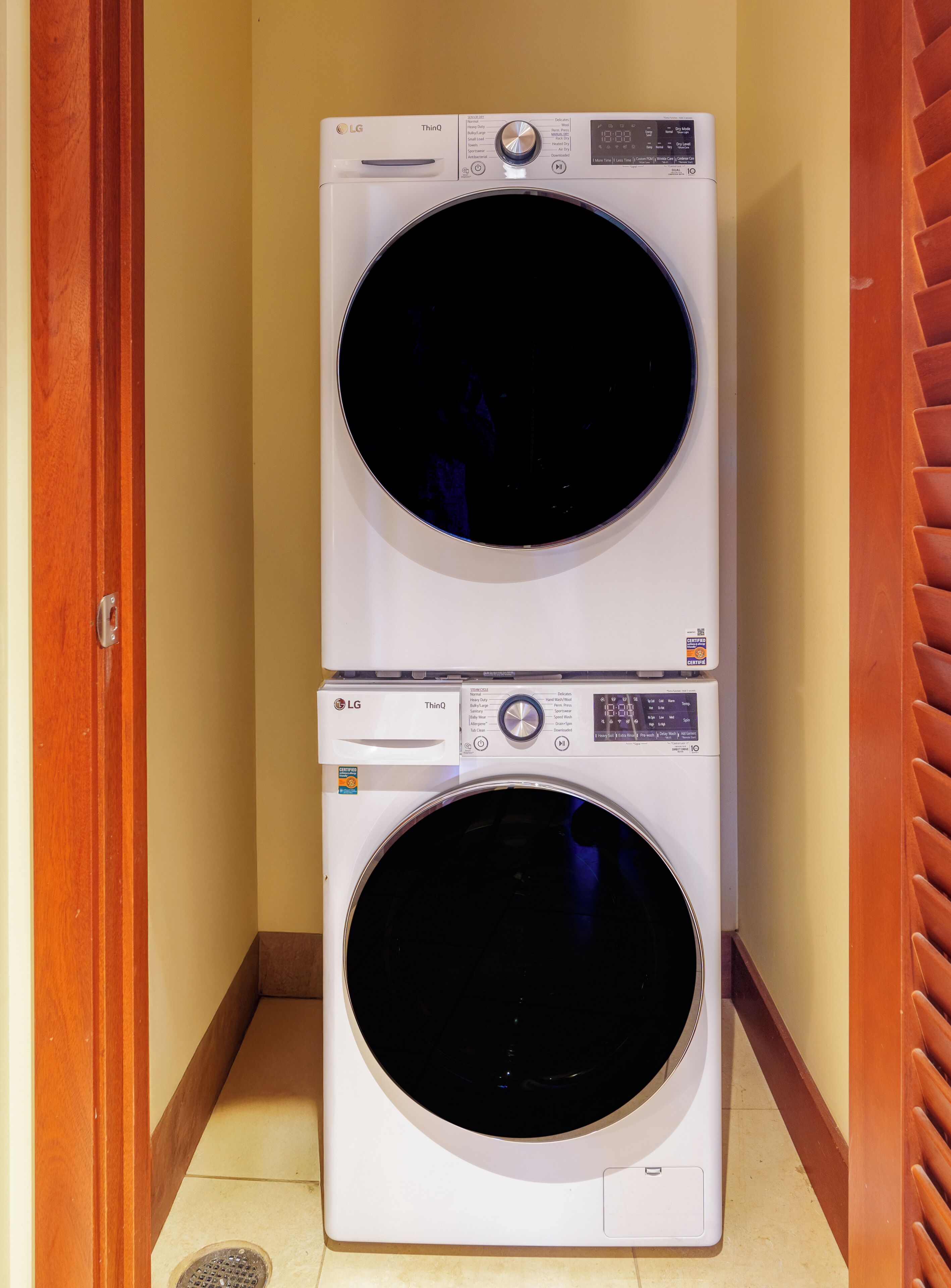 A stacked washer and dryer unit in a hallway with wooden doors and a tiled floor.