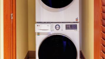 A stacked washer and dryer unit in a hallway with wooden doors and a tiled floor.