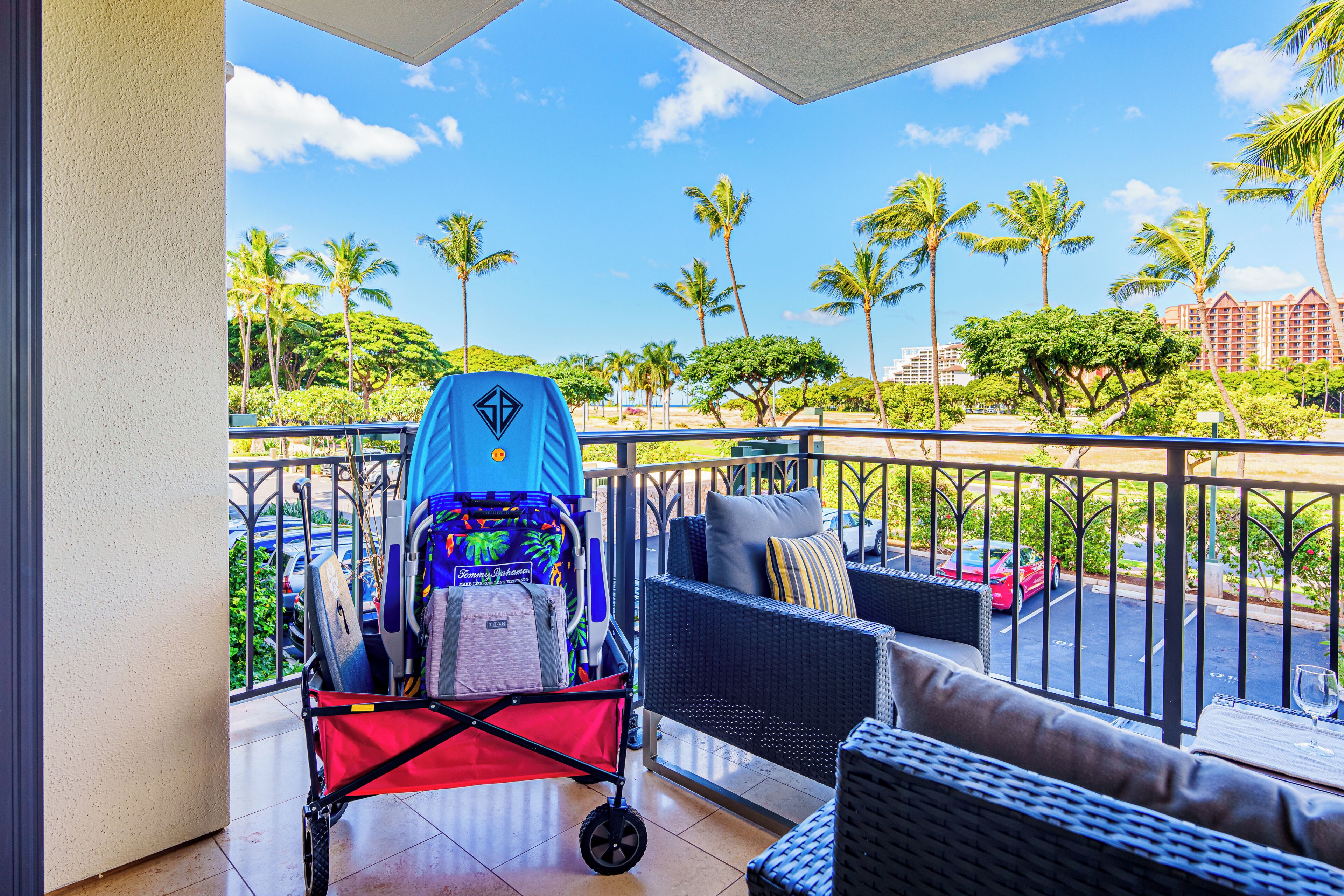 A balcony with a stroller, wicker furniture, and a view of palm trees and a hotel in the background.