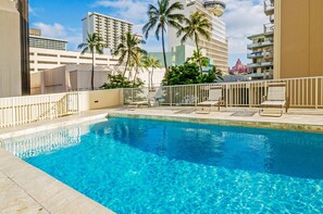A clear blue pool with lounge chairs and palm trees, surrounded by high-rise buildings. - Ocean-city Views at Marine Surf Close to the Beach W/parking & Full Kitchen (Honolulu)