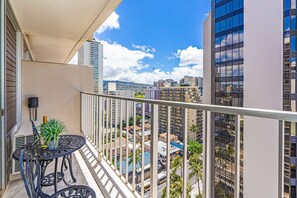 A balcony with a table and chairs, overlooking a cityscape with tall buildings and a clear sky. - Ocean-city Views at Marine Surf Close to the Beach W/parking & Full Kitchen (Honolulu)