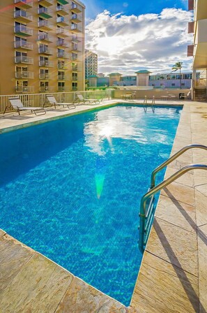 Ein Swimmingpool mit klarem, blauem Wasser, umgeben von Liegestühlen und einer gefliesten Terrasse.