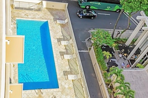 An aerial view of a hotel with a swimming pool, outdoor seating, and a street view with a bus and cars. - Ocean-city Views at Marine Surf Close to the Beach W/parking & Full Kitchen (Honolulu)
