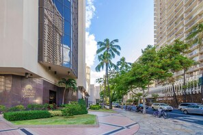 A modern building with a prominent logo, a well-maintained garden, and a street with parked cars and bicycles. - Ocean-city Views at Marine Surf Close to the Beach W/parking & Full Kitchen (Honolulu)