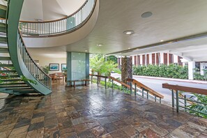 A spacious lobby with a curved staircase, a stone-tiled floor, and a view of the outdoors. - Ocean-marina and Fireworks Views at Ilikai Marina Short Stroll to the Beach (Honolulu)
