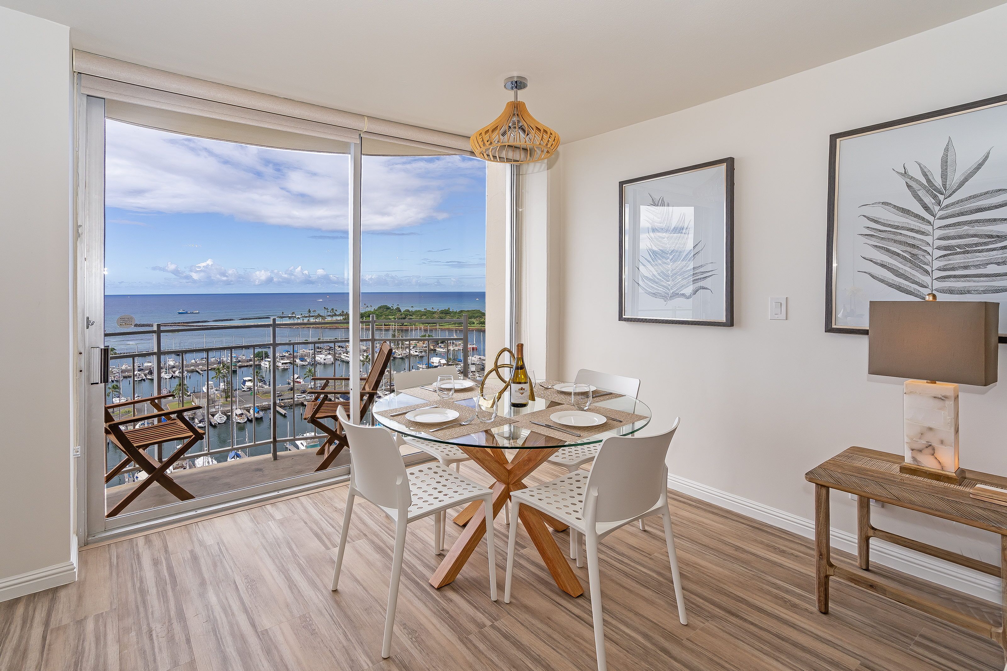 A dining area with a glass table, white chairs, and a view of the marina.