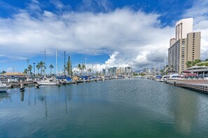 A marina with boats docked, a waterfront promenade, and modern buildings in the background. - Ocean-marina and Fireworks Views at Ilikai Marina Short Stroll to the Beach (Honolulu)