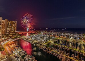 Un port de plaisance avec des bateaux amarrés, une route longeant le bord de l’eau et un bâtiment dont les fenêtres sont illuminées.