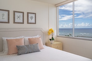 A bedroom with a bed, pillows, a nightstand, a vase with flowers, and framed botanical prints on the wall. - Ocean-marina and Fireworks Views at Ilikai Marina Short Stroll to the Beach (Honolulu)