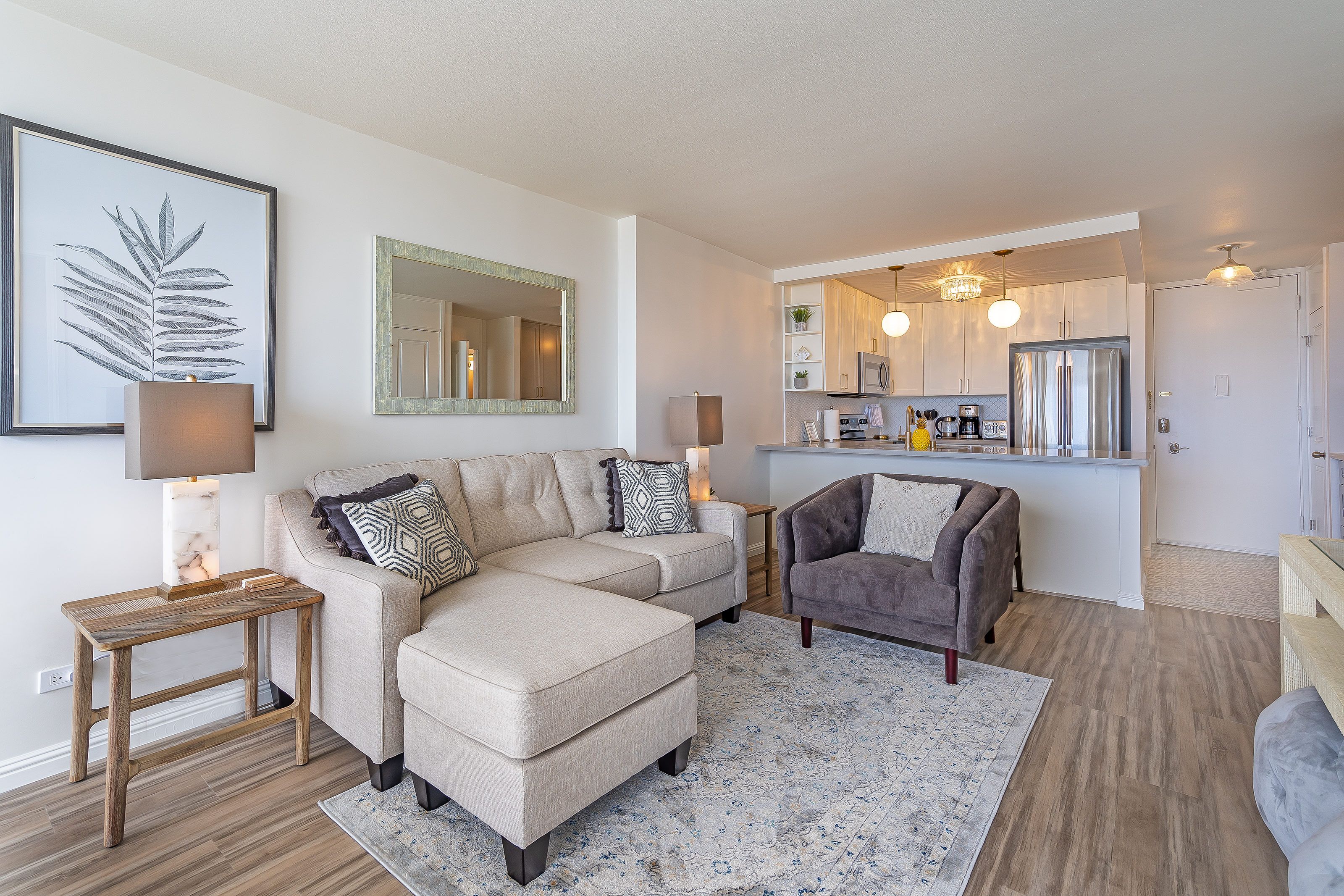 A modern living room with a sectional sofa, a grey armchair, a wooden side table, and a large mirror.