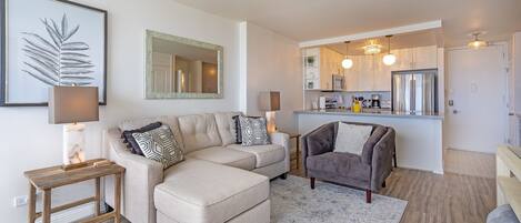 A modern living room with a sectional sofa, a grey armchair, a wooden side table, and a large mirror.
